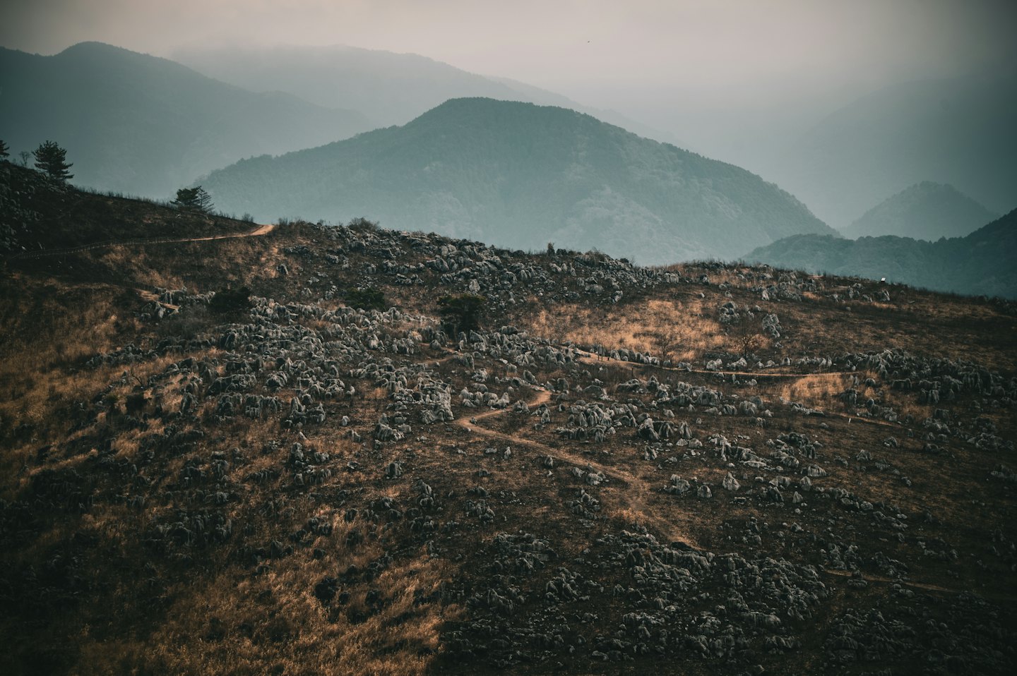 A winding dirt path leads through a rugged mountain landscape.