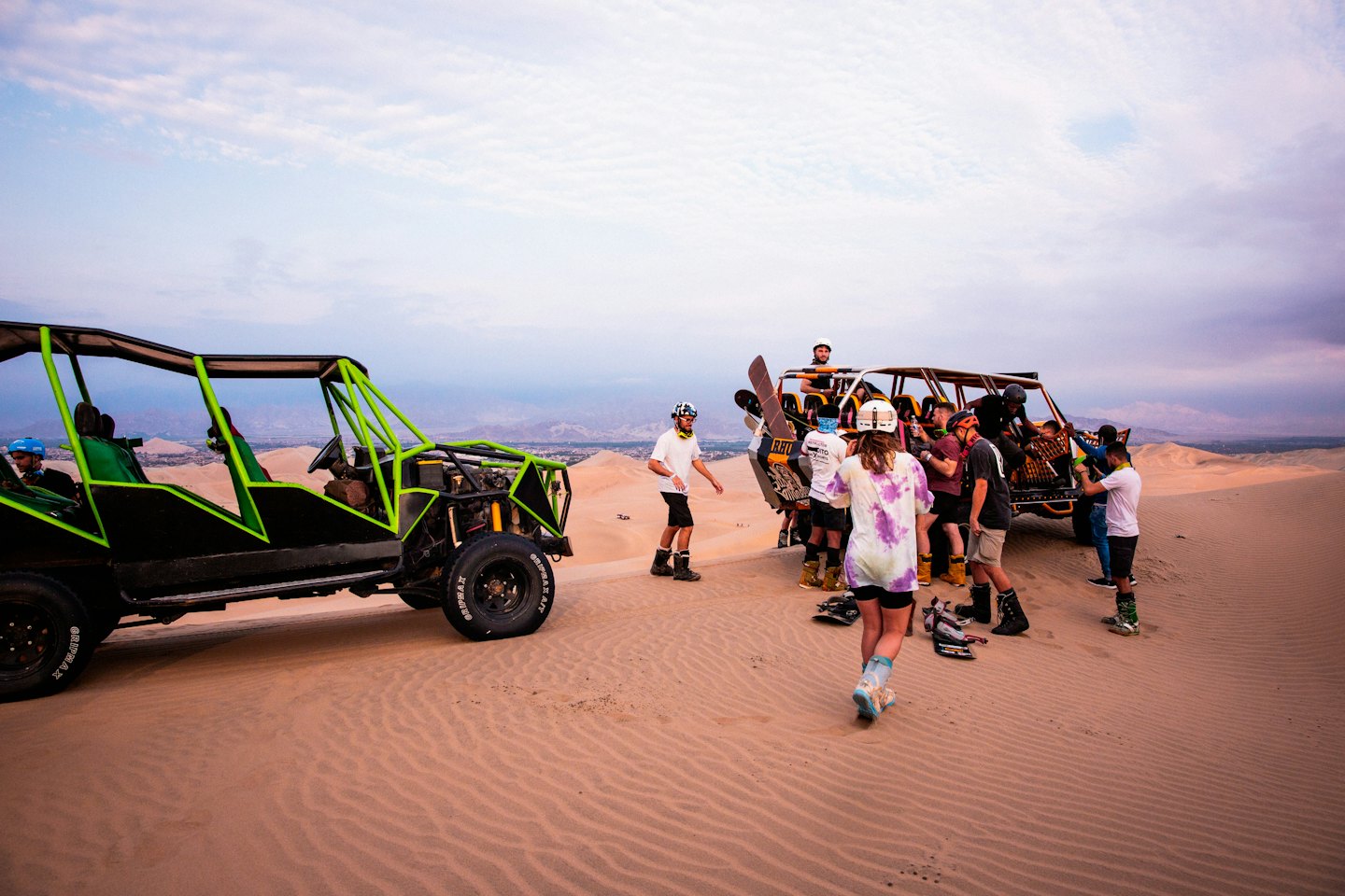 A group gathers near two dune buggies in the desert.